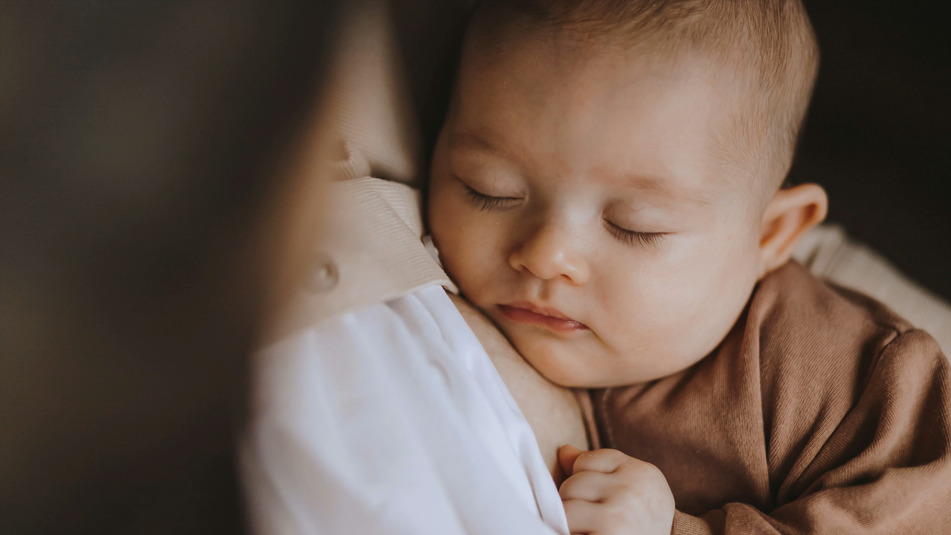 Fyra månaders bebis sover i sin mammas armar