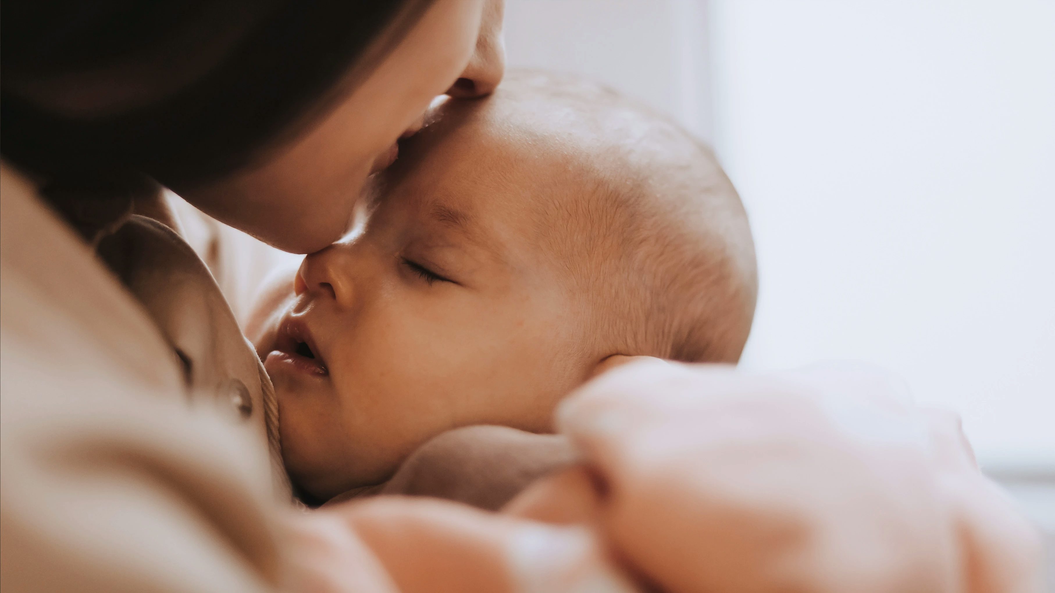 A bother kisses a sleeping baby on the forehead